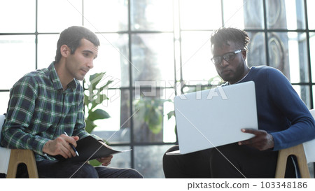 Friendly colleagues chat while sitting in the office, promising young manager shows a presentation on a laptop. 103348186