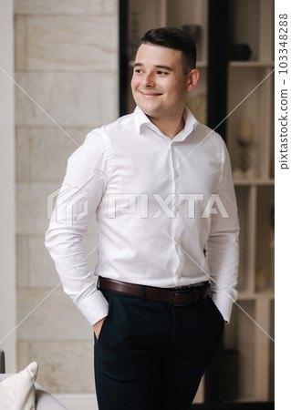 Young groom in white shirt standing by the window and smile Young groom in white shirt standing by the window and smile 103348288