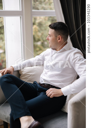Man sitting in front of big window at home. Groom's morning. Wedding day Man sitting in front of big window at home. Groom's morning. Wedding day 103348290