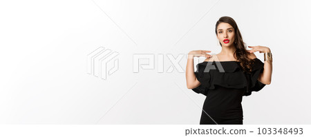 Confident and stylish woman in black elegant dress, looking sassy at camera, standing over white background Confident and stylish woman in black elegant dress, looking sassy at camera, standing over white background 103348493