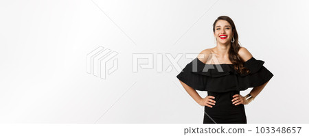 Beauty and fashion concept. Elegant young woman wearing party dress and red lipstick, laughing at camera, standing cheerful against white background 103348657