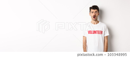 Shocked and confused man in volunteer t-shirt staring at camera speechless, standing against white background Shocked and confused man in volunteer t-shirt staring at camera speechless, standing against white background 103348995