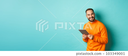Handsome bearded man using digital tablet, laughing at camera, standing happy against light blue background Handsome bearded man using digital tablet, laughing at camera, standing happy against light blue background 103349001