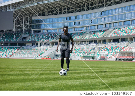 African American man playing football on the stadium field. A man runs with a soccer ball across the field. African American man playing football on the stadium field. A man runs with a soccer ball across the field. 103349107