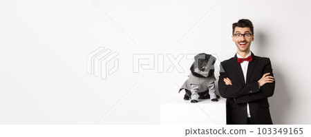 Animals, party and celebration concept. Happy dog owner in suit and puppy in costume looking excited at camera, having fun, standing over white background Animals, party and celebration concept. Happy dog owner in suit and puppy in costume looking excited at camera, having fun, standing over white background 103349165