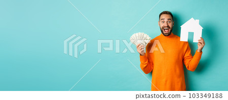 Real estate concept and mortgage concept. Excited man showing dollars and paper maket of house, buying flat, standing over blue background 103349188
