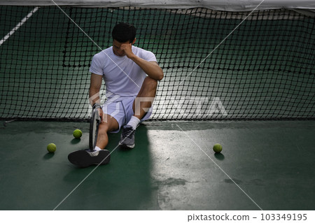 Disappointed asian male tennis player sitting on the court, upset about competition loss, failure emotions Disappointed asian male tennis player sitting on the court, upset about competition loss, failure emotions 103349195