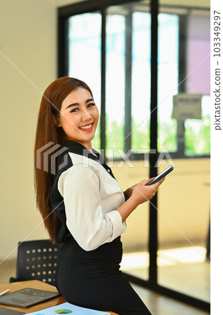 Smiling millennial woman office worker using smartphone, checking social media, communicating online Smiling millennial woman office worker using smartphone, checking social media, communicating online 103349297