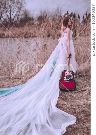 Beautiful romantic european girl with guitar with flowers inside, posing outdoors. Concept of music and nature. Spring time. 103349387