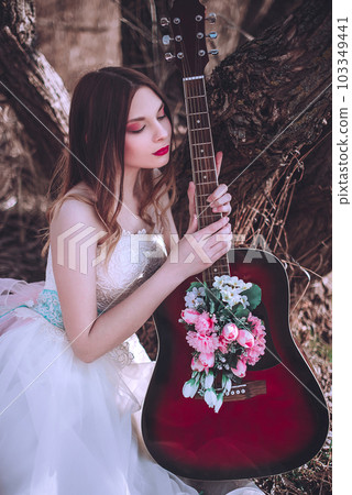 Beautiful romantic european girl with guitar with flowers inside, posing outdoors. Concept of music and nature. Spring time. 103349441