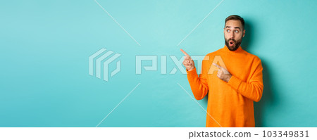 Surprised and curious guy looking at promo, pointing at upper left corner copy space, standing in orange sweater, turquoise background Surprised and curious guy looking at promo, pointing at upper left corner copy space, standing in orange sweater, turquoise background 103349831