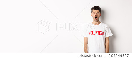 Shocked and confused man in volunteer t-shirt staring at camera and frowning displeased, standing against white background Shocked and confused man in volunteer t-shirt staring at camera and frowning displeased, standing against white background 103349857