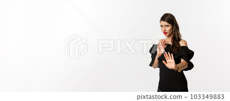 Fashion and beauty. Reluctant and worried woman asking to stay away, showing stop gesture and looking scared, standing in black dress over white background 103349883
