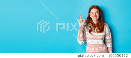 Cute smiling redhead woman showing okay sign, praising good work, well done gesture, standing over blue background Cute smiling redhead woman showing okay sign, praising good work, well done gesture, standing over blue background 103350122