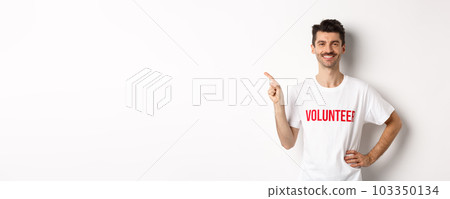 Handsome smiling volunteer in t-shirt pointing finger left, showing announcement, standing over white background Handsome smiling volunteer in t-shirt pointing finger left, showing announcement, standing over white background 103350134