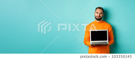 Handsome bearded man in orange sweater showing laptop screen, demonstrating promo, grimacing disappointed and upset standing over light blue background Handsome bearded man in orange sweater showing laptop screen, demonstrating promo, grimacing disappointed and upset standing over light blue background 103350143