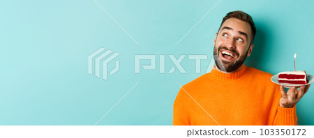 Close-up of happy adult man celebrating birthday, holding bday cake with candle and making wish, standing against turquoise background Close-up of happy adult man celebrating birthday, holding bday cake with candle and making wish, standing against turquoise background 103350172