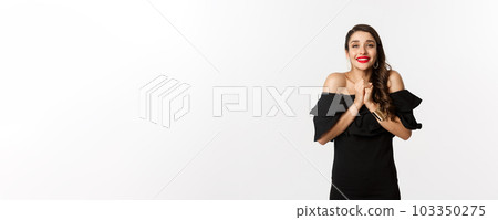 Fashion and beauty. Pretty woman in black dress asking for help, showing thank you gesture, looking grateful at camera, standing over white background Fashion and beauty. Pretty woman in black dress asking for help, showing thank you gesture, looking grateful at camera, standing over white background 103350275