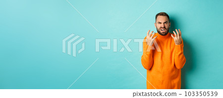 Image of angry man looking disappointed and mad, shaking hands and grimacing with disdain, standing distressed against light blue background Image of angry man looking disappointed and mad, shaking hands and grimacing with disdain, standing distressed against light blue background 103350539