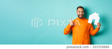 Real estate concept. Satisfied man recommending agency, showing thumb up and house maket, standing over blue background Real estate concept. Satisfied man recommending agency, showing thumb up and house maket, standing over blue background 103350660