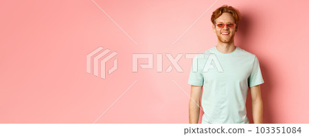Tourism and vacation concept. Cheerful redhead bearded man in sunglasses and t-shirt, smiling and looking happy at camera standing over pink background Tourism and vacation concept. Cheerful redhead bearded man in sunglasses and t-shirt, smiling and looking happy at camera standing over pink background 103351084