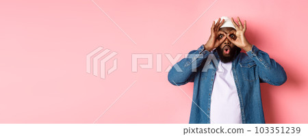 Shocked and impressed african-american guy staring through hand binoculars at camera, seeing amazing promo, standing over pink background Shocked and impressed african-american guy staring through hand binoculars at camera, seeing amazing promo, standing over pink background 103351239