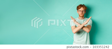 Serious and confident redhead man in t-shirt and glasses saying no, showing cross gesture to stop you, refucing or declining something, standing over turquoise background Serious and confident redhead man in t-shirt and glasses saying no, showing cross gesture to stop you, refucing or declining something, standing over turquoise background 103351242
