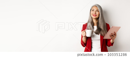 Business people concept. Asian businesswoman drinking coffee and holding digital tablet, smiling thoughtful at upper left corner, white background Business people concept. Asian businesswoman drinking coffee and holding digital tablet, smiling thoughtful at upper left corner, white background 103351286