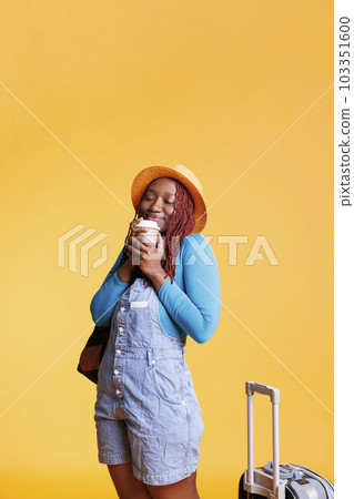 Joyful person enjoying cup of coffee in studio, having trolley bags to leave on holiday destination. Female tourist drinking beverage for international flight weekend activities. Joyful person enjoying cup of coffee in studio, having trolley bags to leave on holiday destination. Female tourist drinking beverage for international flight weekend activities. 103351600
