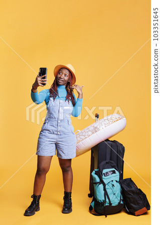 African american woman on videocall chat in studio, talking to someone on online teleconference. Young tourist chatting on remote videoconference, travelling on vacation journey. 103351645