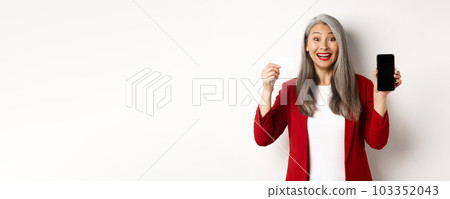 Cheerful asian mature woman showing blank smartphone screen and credit card, concept of e-commerce 103352043