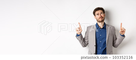 Skeptical and hesitant young businessman in suit looking up with disappointed smirk, feel unsure about deal, standing dissatisfied on white background Skeptical and hesitant young businessman in suit looking up with disappointed smirk, feel unsure about deal, standing dissatisfied on white background 103352116