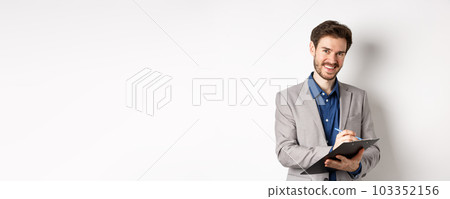 Smiling male manager in suit writing on clipboard, taking notes at office meeting, standing on white background Smiling male manager in suit writing on clipboard, taking notes at office meeting, standing on white background 103352156