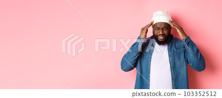 Distressed Black man having headache, touching head and grimacing with concerned face, standing over pink background 103352512