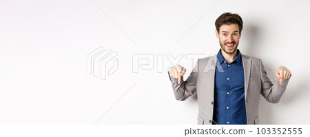 Hey check this out. Happy businessman in suit pointing fingers down and smiling, inviting to event, showing link, standing on white background Hey check this out. Happy businessman in suit pointing fingers down and smiling, inviting to event, showing link, standing on white background 103352555