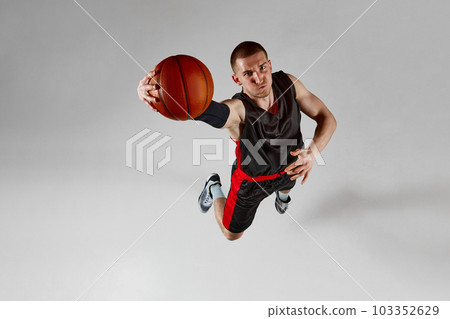 Concentrated sportsman, male basketball player in motion, jumping with ball against grey studio background. Top view 103352629