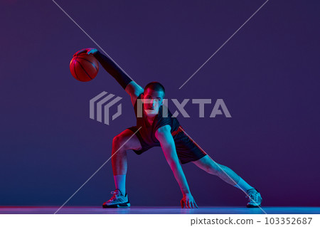 Concentration and motivation. Young man, basketball player in motion with ball against purple studio background in neon light. 103352687