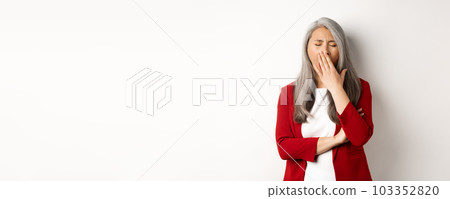 Tired or bored asian businesswoman yawning, covering mouth with hand, standing exhausted over white background Tired or bored asian businesswoman yawning, covering mouth with hand, standing exhausted over white background 103352820