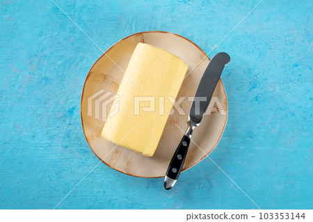 A stick of butter with a knife on a plate, overhead flat lay shot on blue 103353144