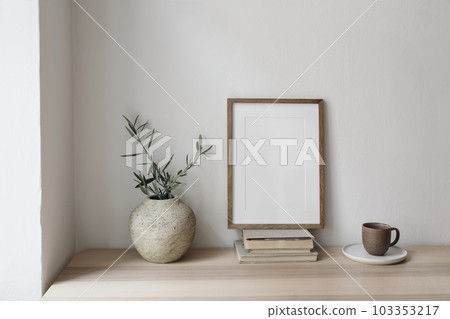 Cup of coffee, books. Empty vertical picture frame mockup on old books. Wooden desk, table. Vase with olive branches. Elegant working space, home office concept. Summer interior design. Breakfast. 103353217