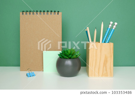 School equipment on white table, green wall background. Education backdrop. Wooden school supplies, notepad, pencils and cactus plant. Back to school. Student Desk. Stationery for study. Work at home School equipment on white table, green wall background. Education backdrop. Wooden school supplies, notepad, pencils and cactus plant. Back to school. Student Desk. Stationery for study. Work at home 103353486