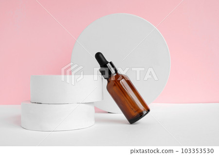 Amber glass dropper cosmetic bottle, white podium. Natural skin care SPA beauty product design. Mineral organic oil on pink background. Mock-Up. Oily pipette. Face and body treatment. Front view 103353530