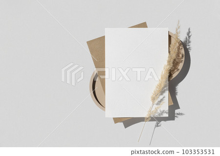 Blank greeting card, invitation mockup. Dry grass, pampas plant on white table background. Flat lay, top view. Copyspace. Blank paper cards, mock up. Modern Minimal business brand template. A6 103353531