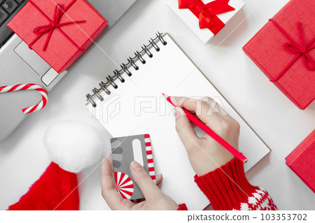 Christmas online shopping flat lay. Girl writing shopping list. Female Hands with Credit card and Pencil. Laptop and christmas presents on white table. Copy space. Winter holidays sales 103353702