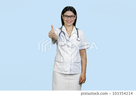 Portrait of a young female asian doctor showing like gesture. Wearing stethoscope and glasses. Isolated on pale blue. Portrait of a young female asian doctor showing like gesture. Wearing stethoscope and glasses. Isolated on pale blue. 103354214