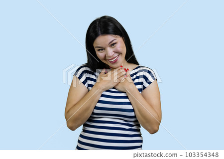 Grateful young asian woman touching her heart and saying thank you. I'm so thankful. Receiving help and love. Isolated on blue. 103354348