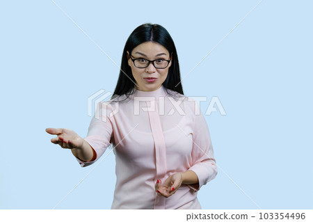Portrait of a young female asian boss in glasses is giving you an order. Isolated on pale blue. Portrait of a young female asian boss in glasses is giving you an order. Isolated on pale blue. 103354496