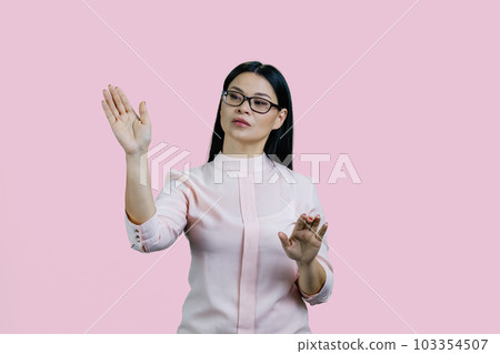 Young asian businesswoman is swiping an invsible touch screen. Isolated over pink background. Young asian businesswoman is swiping an invsible touch screen. Isolated over pink background. 103354507
