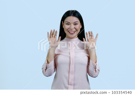 Young asian woman with her hands up shows her palms. Give up gesture. Isolated on pale blue background. 103354540