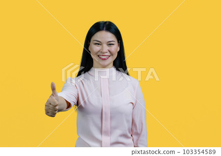Portrait of a young happy cheerful asian woman is giving a thumb up. Isolated on yellow background. Portrait of a young happy cheerful asian woman is giving a thumb up. Isolated on yellow background. 103354589